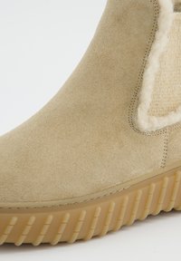 Beige semišové kotníkové boty s texturovaným povrchem a kožíškovou podšívkou, s gumovou podrážkou s rýhovanými detaily pro lepší trakci.