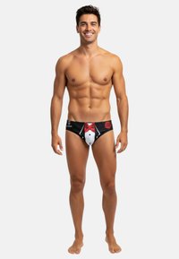 Culottes de bain noires avec un design de smoking, comprenant une chemise blanche et un nœud papillon rouge. Fabriquées en matériau lisse, accentuées par un motif de rose.