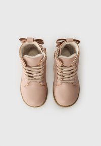 Bottines en cuir rose avec un design à lacets, doublure douce et nœuds décoratifs à l'arrière. Elles possèdent une semelle en caoutchouc marron et des accents en vagues.