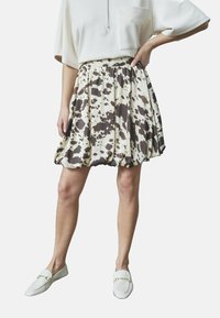 En knælang nederdel lavet af letvægtsstof med en beige bund, der har brune abstrakte pletter og en samlet talje.