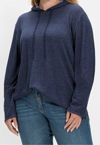 Marineblaue Kapuzenjacke aus strukturiertem Stoff, mit langen Ärmeln, verstellbarem Kapuzenzug und lockerer Passform, kombiniert mit Denim-Jeans.