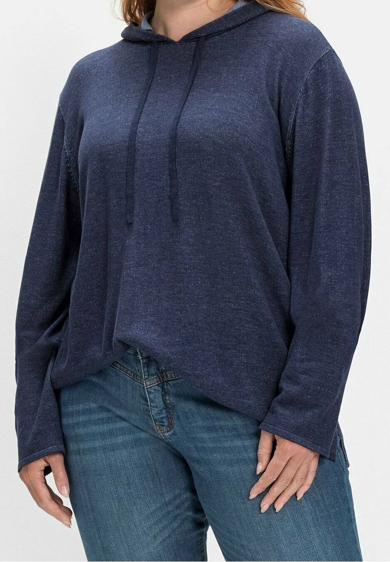 Marineblaue Kapuzenjacke aus strukturiertem Stoff, mit langen Ärmeln, verstellbarem Kapuzenzug und lockerer Passform, kombiniert mit Denim-Jeans.