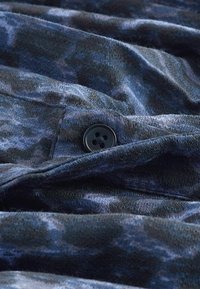 Námorně modrý látka s měkkou texturou, s černým knoflíkem a jemnými vzory. Materiál se zdá být mírně pomačkaný.