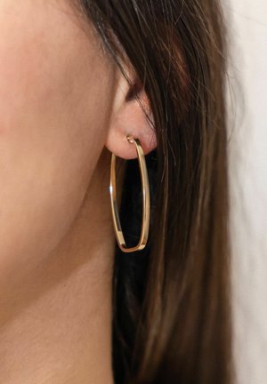 Close-up of ear with sleek, rectangular gold hoop earring worn by person with brown hair.
