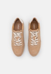 Beige suede sneakers with a textured finish, white accents, and patterned laces. Features a cushioned insole and elongated toe design.