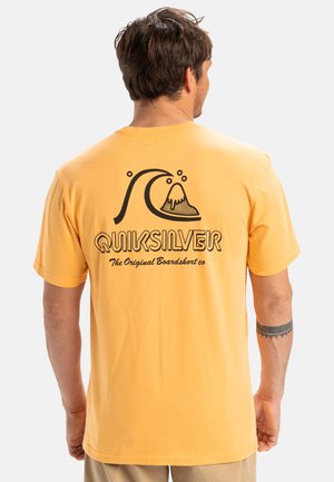 Geel katoenen T-shirt met een zwarte grafiek van een golf en berg, met daaronder de tekst "QUIKSILVER". Korte mouwen en een ontspannen pasvorm.