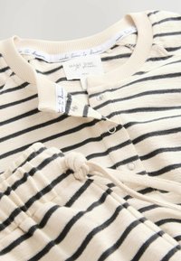 Pajama set z ramenskimi črtami v bež in črni barvi, z zapenjanjem na gumb in hlačami na vrvico. Mehka tkanina z rebrasto teksturo in subtilnimi oznakami blagovne znamke.