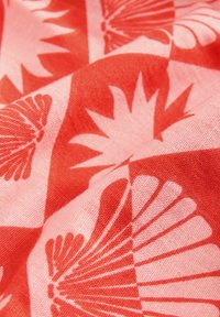 Tessuto rosso e rosa con motivo geometrico a conchiglia e foglia, caratterizzato da una texture liscia e un aspetto morbido e intrecciato.