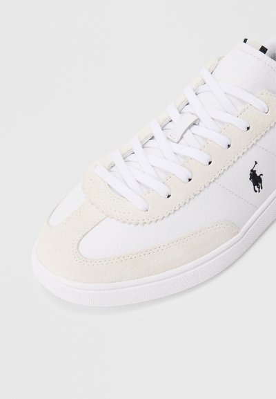 Ténis branco com detalhes em camurça e atacadores brancos, apresentando um logótipo de jogador de polo preto no lado e uma sola de borracha texturada.