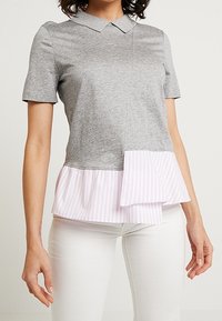 Top grigio a maniche corte con colletto. Presenta un orlo peplum a righe rosa, una texture liscia e una vestibilità rilassata.