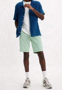 Niebieska koszula krótki rękaw w białe wzory, zestawiona z miętowymi szortami. Biała koszulka pod spodem i szare sneakersy z akcentami.