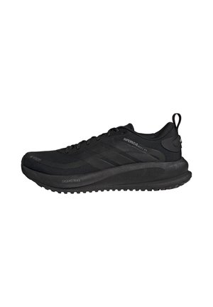 Chaussure de sport noire basse avec semelle épaisse, design à lacets, grip texturé et détails de marque sur le côté et la boucle du talon.