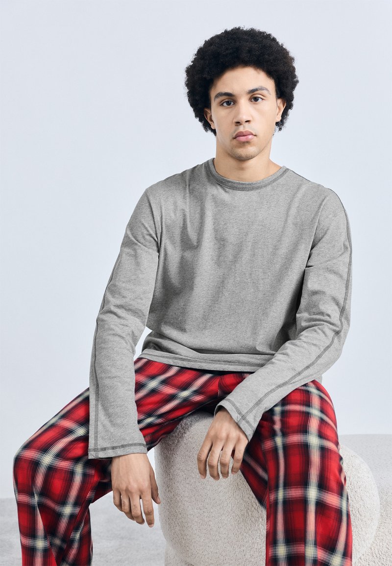 Gray long-sleeve shirt with a crew neck, paired with red plaid pajama pants featuring white and blue accents, sitting on a textured round stool.