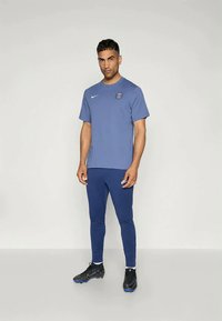 Nike sporta apģērbs, kas sastāv no zila īsām piedurknēm krekla, tumši ziliem pieguļošiem biksēm un melnām futbolu apaviem ar zila akcentiem.