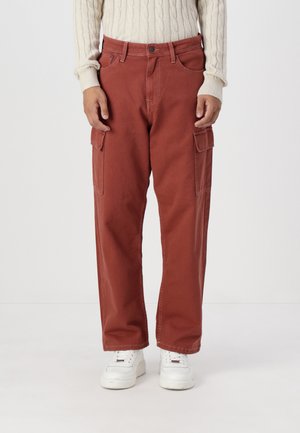 Pantalons cargo de couleur rouille, en coton. Dotés de deux poches latérales, d'une coupe décontractée et d'une longueur courte, associés à des baskets blanches.