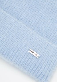 Gorro de punto azul claro con textura suave, con costillas verticales y una etiqueta de metal con el logo "WITTCHEN".