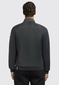 Black zip-up jacket with a smooth texture, fitted design, and raglan sleeves. Features a logo patch on the collar and ribbed cuffs.