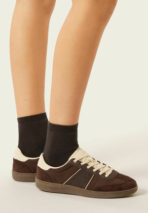 Scarpe in suede marrone e tela con accenti beige, design con lacci e suola in gomma, indossate con calzini neri sopra la caviglia.