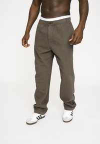 Khaki bomuldsbukser med en afslappet pasform, elastisk talje og knaplukning. Kombinationen med hvide sneakers med sorte striber.