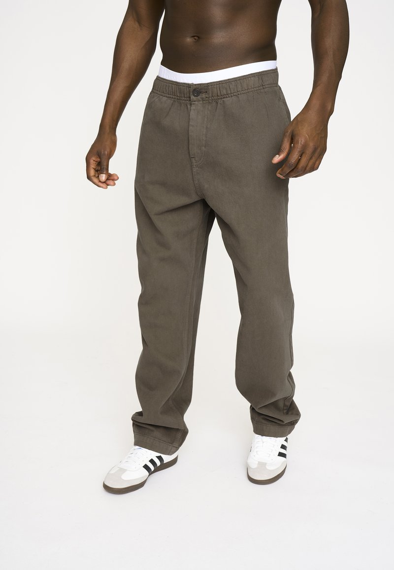 Khaki bomuldsbukser med en afslappet pasform, elastisk talje og knaplukning. Kombinationen med hvide sneakers med sorte striber.