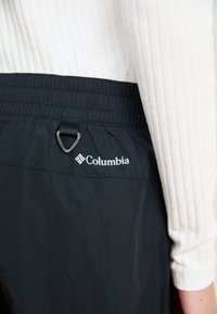 Svart Columbia-bukser med elastisk midje, med en løkke-detalj og Columbia-logoet i hvitt. Glatt, lett materiale.