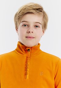 Oranje fleece sweatvest met een hoge kraag, halve rits en een logo aan de voorkant. Zachte textuur met een gladde afwerking en minimale details.
