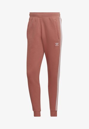 Pantalon de survêtement Adidas couleur rouille avec taille élastique, trois bandes blanches sur les côtés, chevilles resserrées, poches latérales et petit logo sur la cuisse gauche.