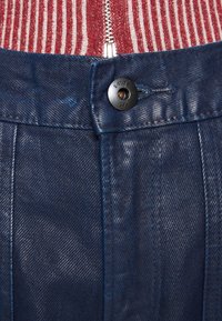 Navy blue denim pants featuring a metal button closure, textured fabric, and visible stitching details. Zippered maroon striped top above.