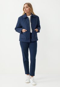 Giacca imbottita blu navy con colletto, bottoni frontali e due tasche. Abbinata a pantaloni coordinati e sneaker bianche per un look armonioso.