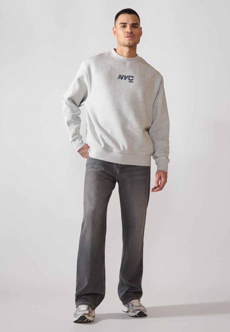 Szara bluza z nadrukiem "NYC", skomponowana z ciemnoszarymi dżinsami. Cechy to okrągły dekolt, długie rękawy oraz fakturowany materiał.