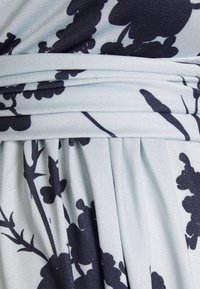 Tecido com padrão floral em azul claro com flores em azul marinho escuro, apresentando um design plissado e uma cintura franzida. Material suave e texturizado.