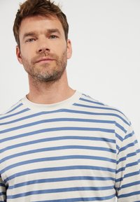 Stripete t-skjorte laget av mykt stoff, med brede blå og hvite horisontale striper, rund hals og korte ermer.