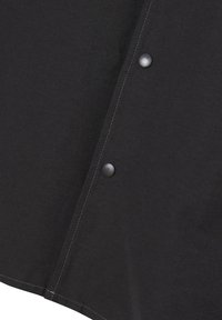Black garment with visible stitching. Features snap fasteners, flat collar, and a slightly curved hem. Fabric appears smooth with a matte finish.
