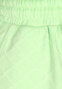 Világos zöld, textúrált anyag, amelyet gyémántmintázat díszít, és összegyűjtött derékrésze van. A felülete puha és kissé plüssös hatású.