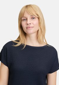 Haut bleu marine à manches courtes en tissu texturé, avec un col rond et une coupe décontractée. Aucun motif visible ni détail en métal.