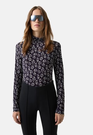 Long-sleeve top with a purple base and white geometric pattern; paired with high-waisted black pants. Accentuated by sleek sunglasses.