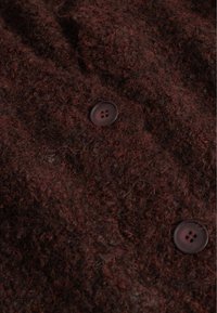 Detailní záběr tmavě hnědé chlupaté vlněné tkaniny se dvěma tmavými kulatými knoflíky přišitými na ní.