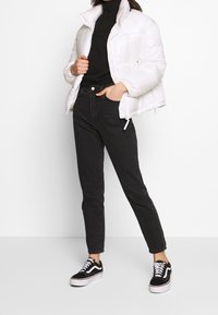 White puffer jacket with a high collar, paired with black high-waisted jeans and black Vans sneakers with white accents, featuring laces.
