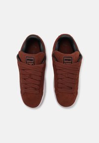 Braune Wildledersneaker mit dicken Schnürsenkeln, runder Spitze, schwarzem Innenfutter und weißer Gummisohle. Mit einem kleinen Logo an der Seite.