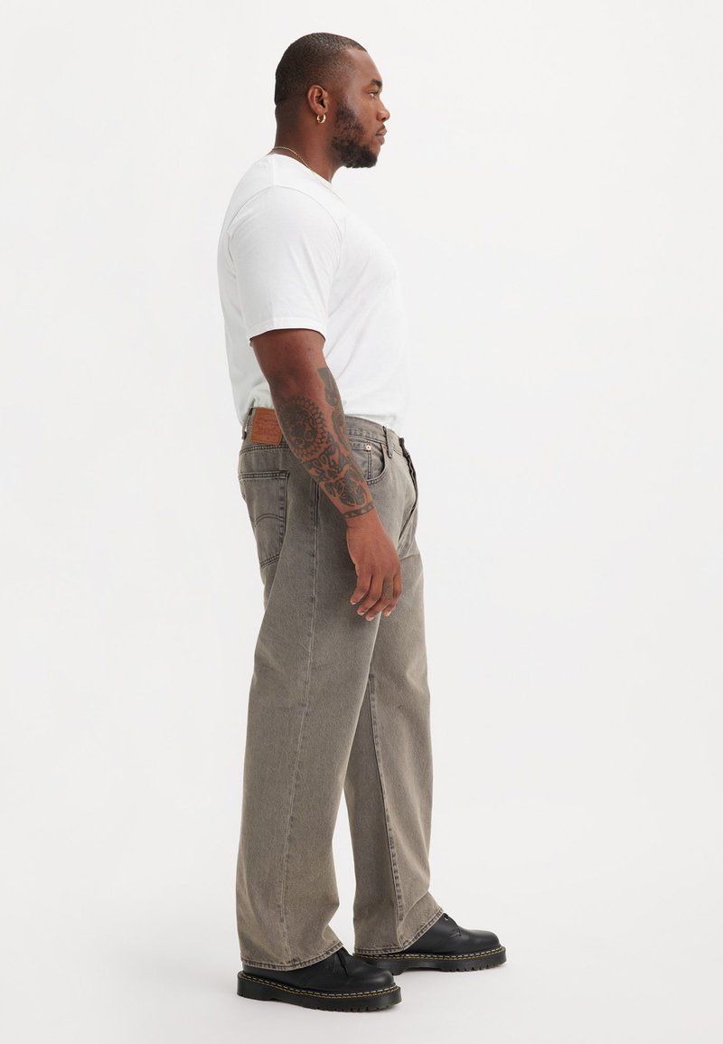 Jean large gris avec une texture de denim moyen, associé à un t-shirt blanc et des chaussures à plateforme noires, avec un patch en cuir à l'arrière.