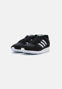 Černé sportovní boty kombinující jemnou kůži a syntetické materiály. Tři bílé pruhy na boku, bílá podrážka a texturovaný vzorek.