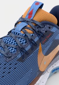 Blauwe en oranje Nike trailrunning schoenen met gestructureerd mesh, een golvend blauw patroon en een opvallend oranje swooshlogo.