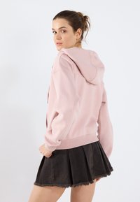 Sweatshirt à capuche rose en tissu doux avec des poignets côtelés, associé à une jupe en denim noir avec un ourlet effiloché et un design plissé.