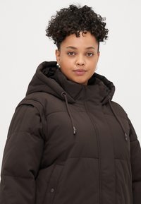 Brown puffer jacket with a thick hood, visible stitching, and side pockets. Features a drawstring at the hood for adjustable fit.