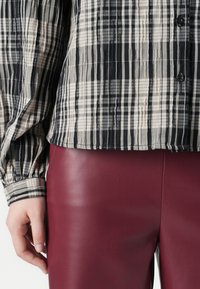 Zwart-wit geruite button-up shirt van textuurstof met gathered cuffs, gecombineerd met burgundy leren broek die een gladde glans toont.