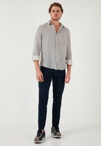 Cămașă cu dungi, cu mâneci lungi, pantaloni bleumarin și adidași gri. Cămașa are o croială lejeră și un material ușor.
