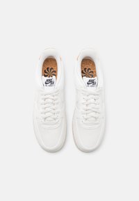 White Nike Air Force 1 sneakers with textured fabric, flat laces, and cork insole. Classic round toe and slight brown accents on the heel.