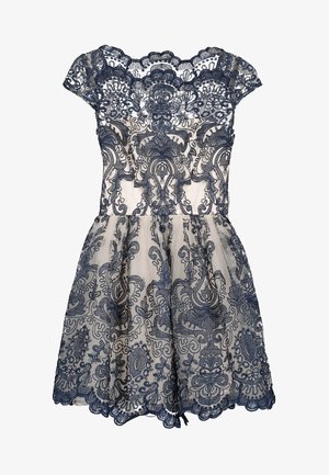 Beige jurk met korte mouwen en een verfijnde overlay van marineblauwe kant met bloemmotieven en ornamentale patronen.