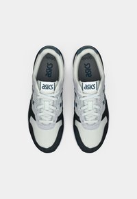 Białe i granatowe buty sportowe z siateczkową cholewką, zaokrąglonym noskiem i płaską podeszwą. Zawierają sznurówki oraz wyściółkę przy języku i kołnierzu. Widoczne logo marki.