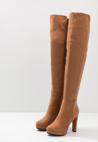 Brązowe zamszowe kozaki za kolano na wysokim obcasie z platformą, z bocznym zamkiem błyskawicznym i gładką fakturą.